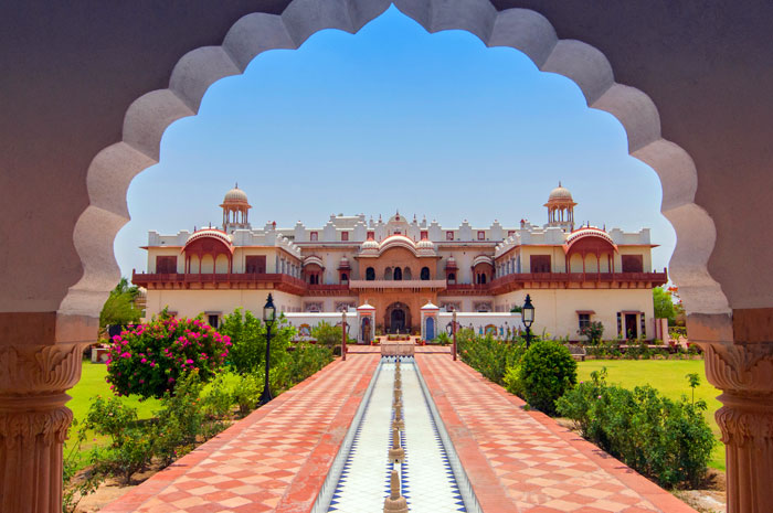 Historic Bharatpur Palace framed by arched stone pillars, featuring a central pathway, fountain pool, and landscaped gardens