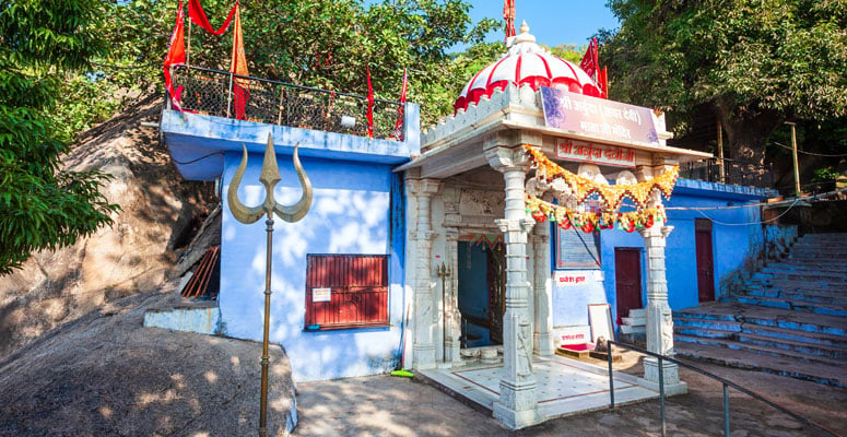 Exterior view of Adhar Devi Temple built into a rocky hill with blue walls and trident in Mount Abu