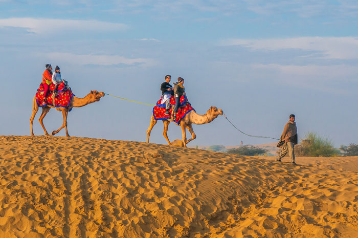 Tourists riding camels across the Thar Desert sand dunes in Rajasthan